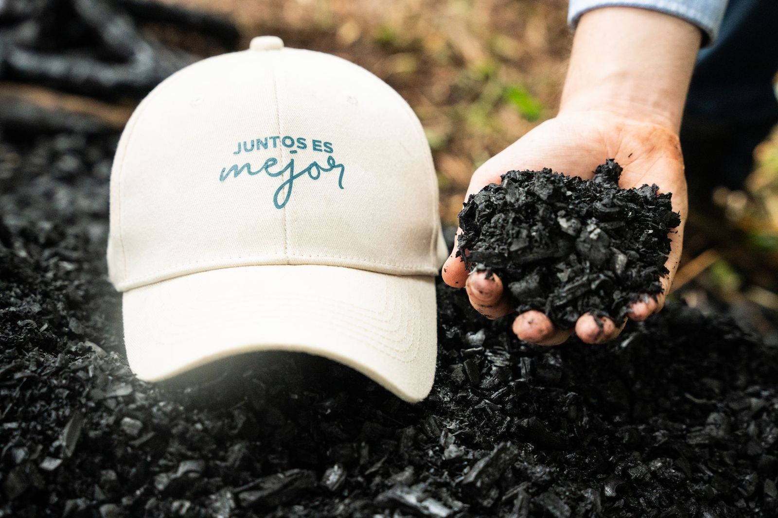 Two hands together holding freshly made biochar, broken into pieces, over the ground of a coffee farm