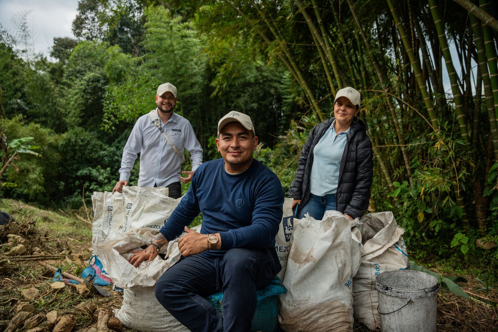 Three of the Cirkular team resting on sacks of biochar at the edge of a farm, with a stand of guadua behind them