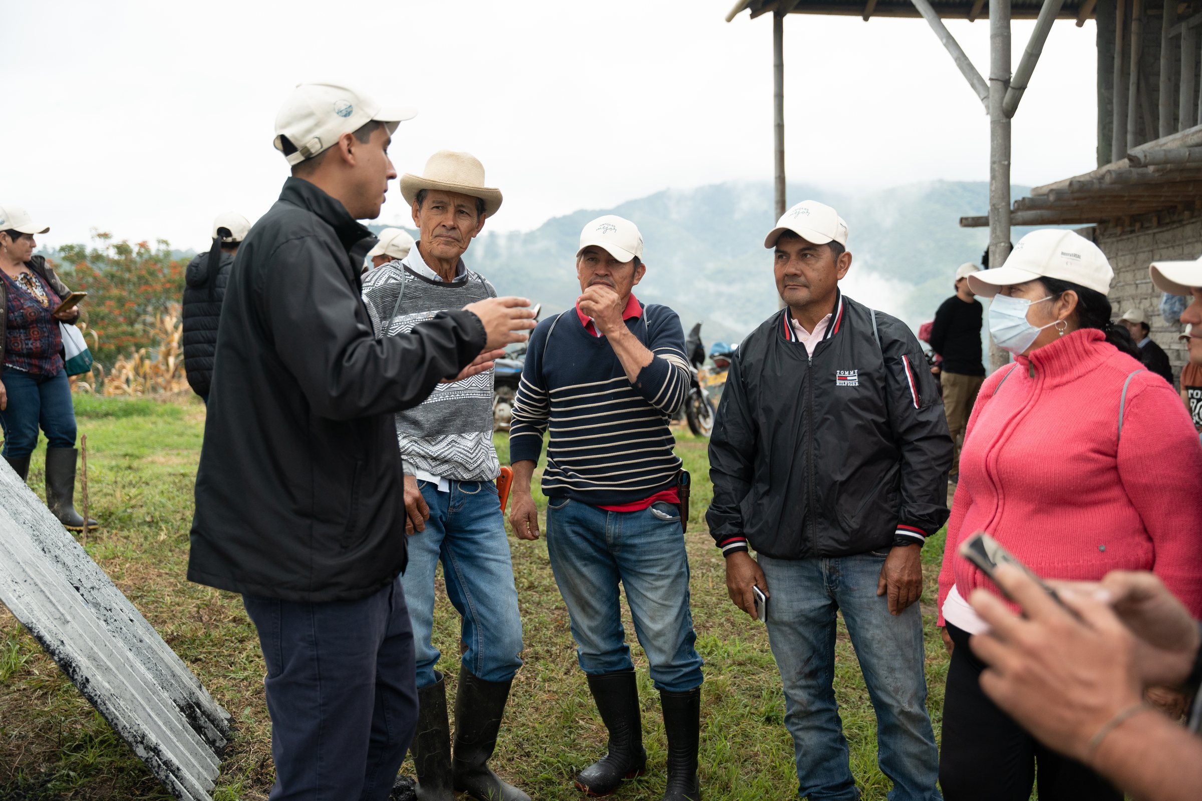 A field school on a farm in the program: four cafeteros in work caps and rubber boots listening to a Cirkular technician, the Andean ridge behind them