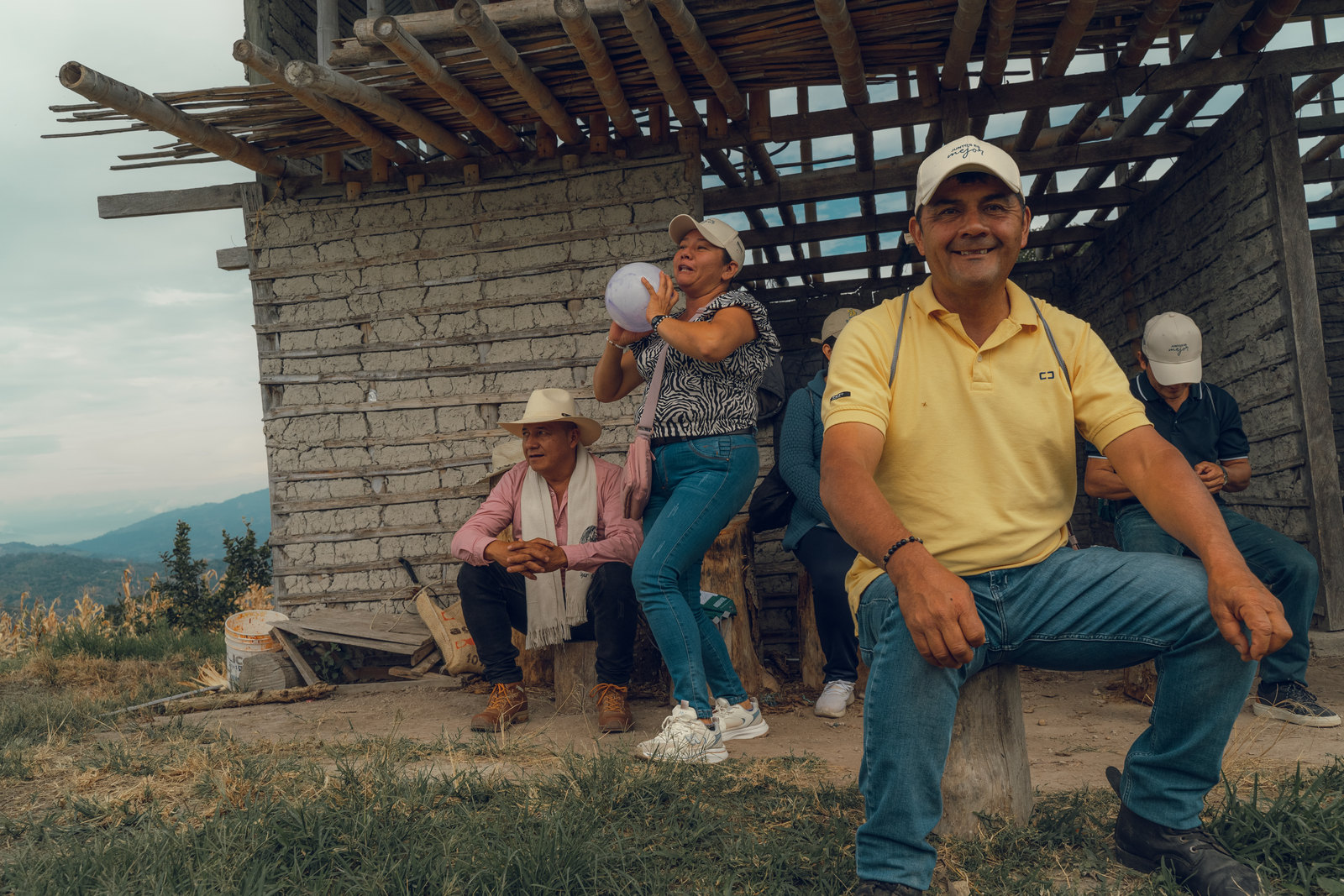 Growers in the program resting together under an open timber shelter on a ridge, one of them smiling at the camera, with the Andean range behind