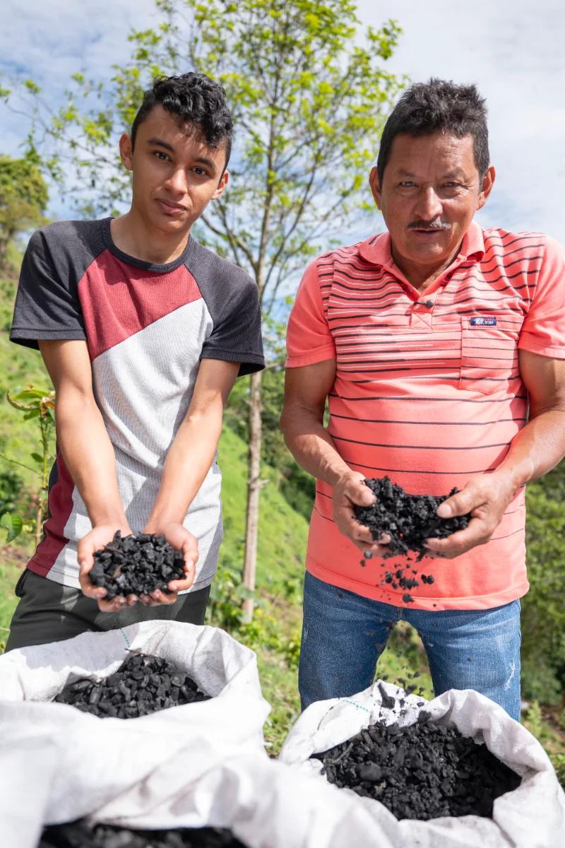 Fabio Mora Rivera and his son Jason holding handfuls of biochar above open sacks on their farm