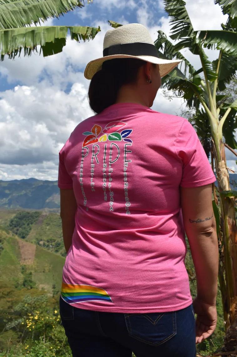 Paola Conde walking away from the camera between banana and coffee plants, wearing a Pride Coffee shirt and a sun hat