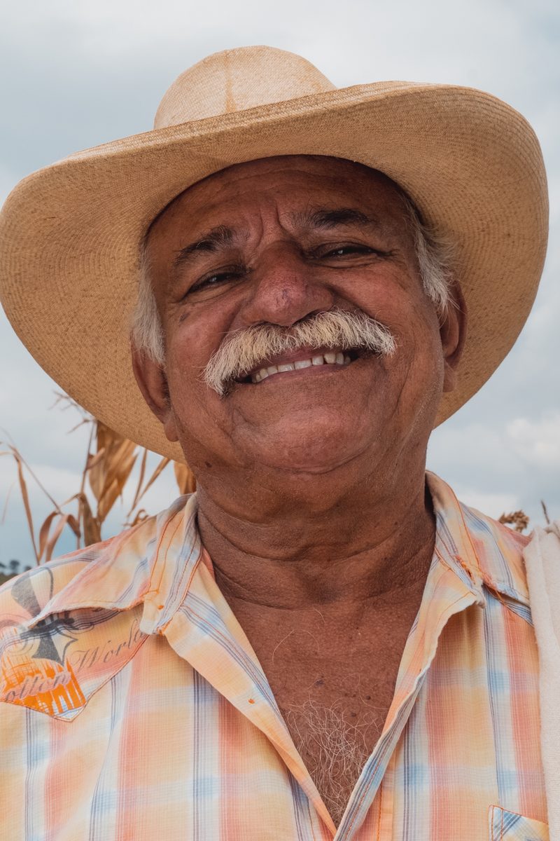 A coffee grower in the program in a straw hat, dry maize stalks beside him