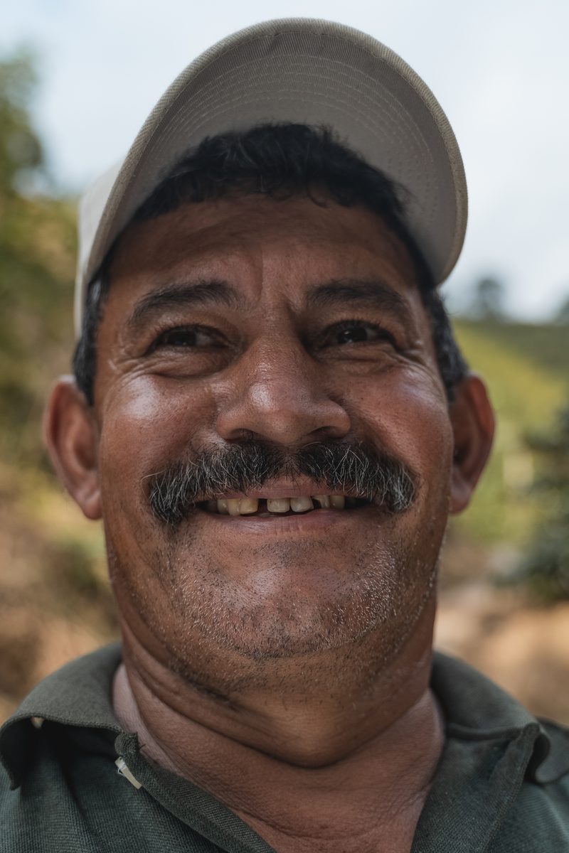 A coffee grower in the program, close, the hillside of his farm behind him