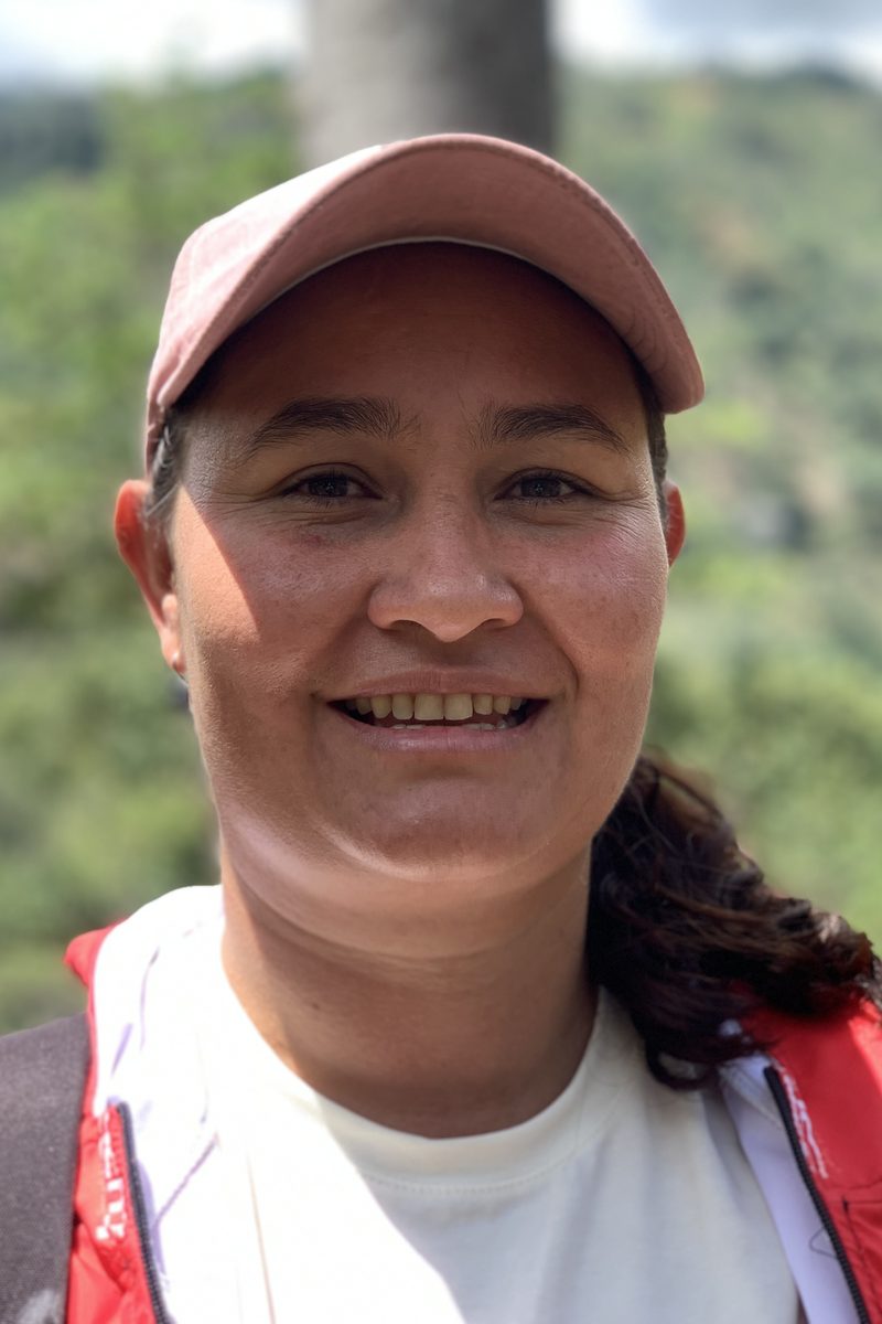 A woman coffee grower in the program on her own farm, the hillside behind her